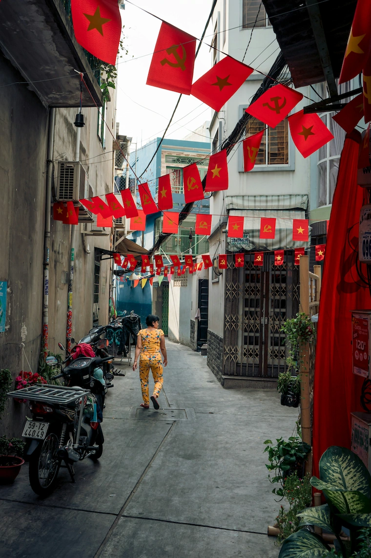 Saigon alley with red flags overhead and a woman walking in floral pajamas