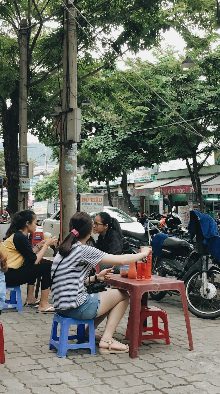 Women on plastic stools at a sidewalk hủ tiếu stand